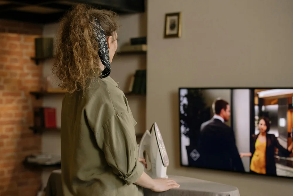 Kobieta prasuje oglądając telewizję